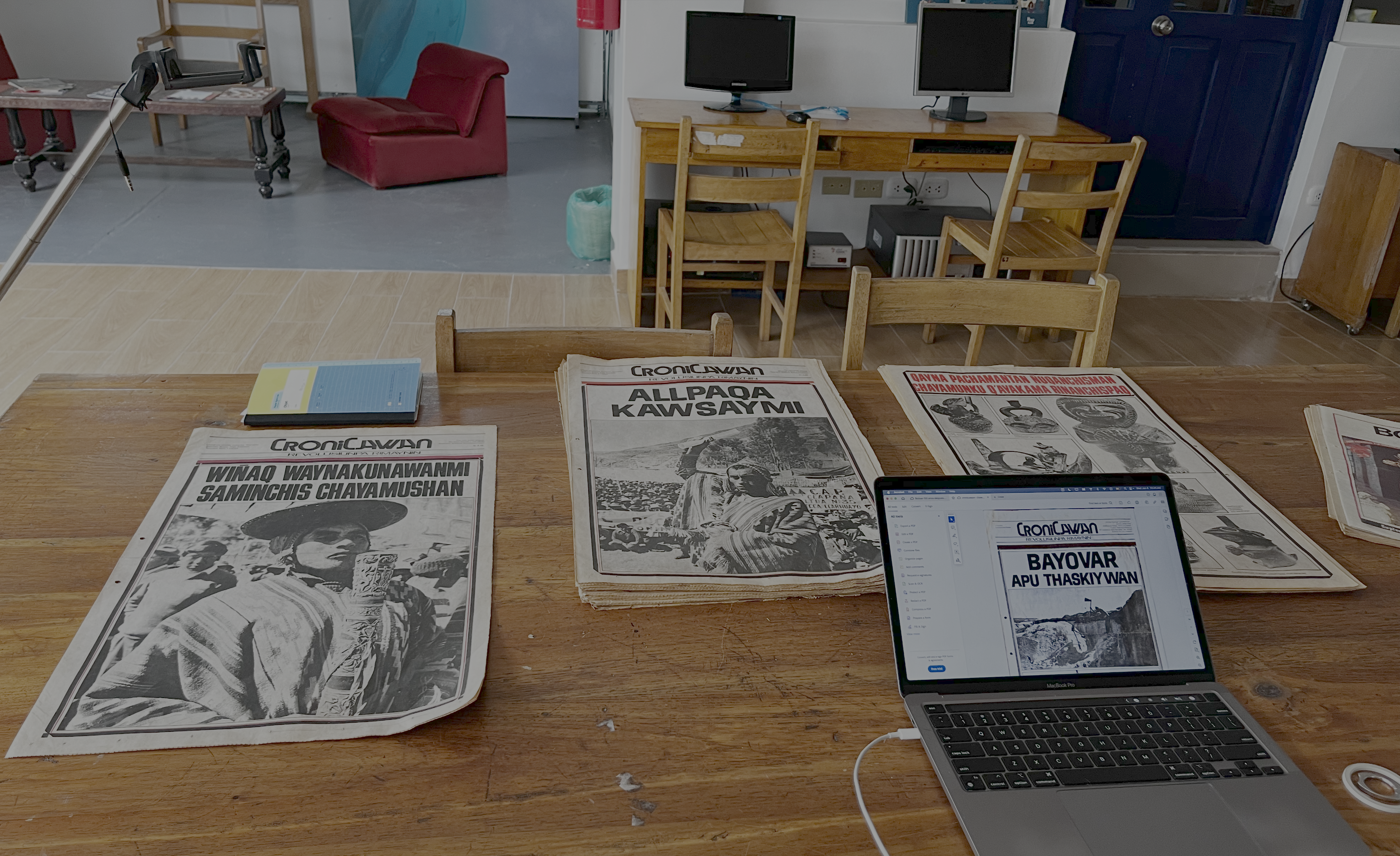 A photo of the digitization setup, including a table, copies of the newspapers, a tripod, and a laptop showing scans of the issues.